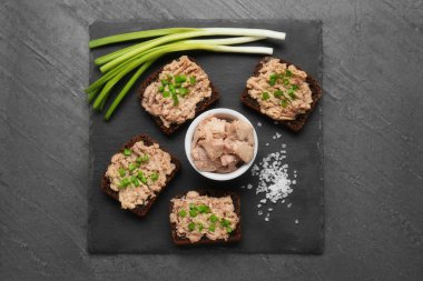 Tasty sandwiches with cod liver, salt and green onion on grey table, top view