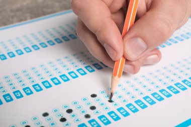 Student filling answer sheet at table, closeup. Passing exam