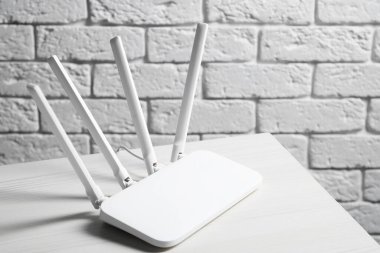 New Wi-Fi router on white wooden table against brick wall. Space for text