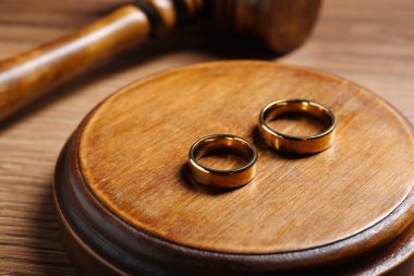 Divorce process. Wedding rings near gavel on wooden table, closeup