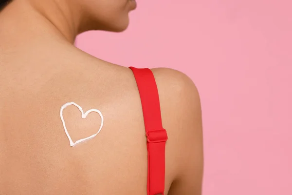 Young woman with sun protection cream on her back against pink background, closeup. Space for text