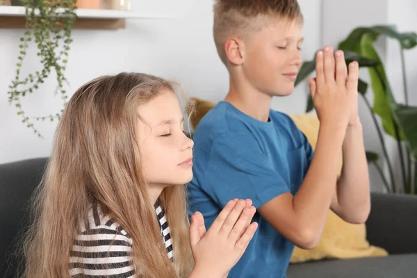Children with clasped hands praying on sofa at home