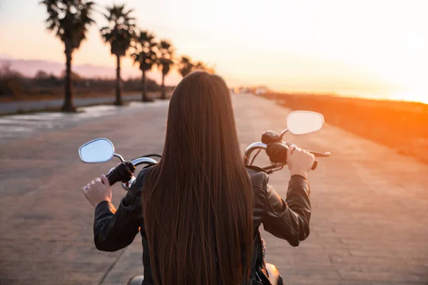 Woman riding motorcycle at sunset, back view