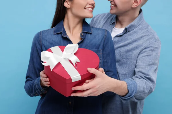 Boyfriend presenting gift to his girlfriend on light blue background, closeup