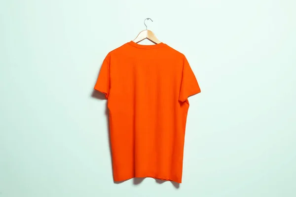 Hanger with orange t-shirt on light wall. Mockup for design