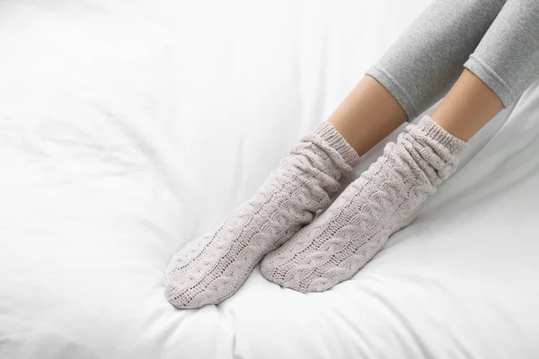 Woman wearing warm socks in comfortable bed, closeup. Space for text