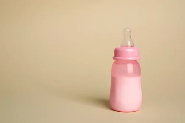 Feeding bottle with infant formula on beige background. Space for text