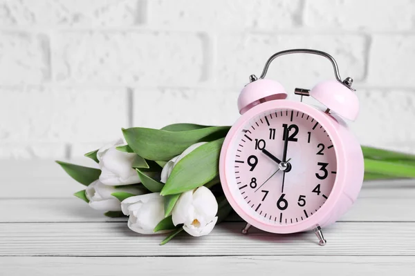Pink Alarm Clock Beautiful Tulips White Wooden Table Brick Wall — Stok fotoğraf