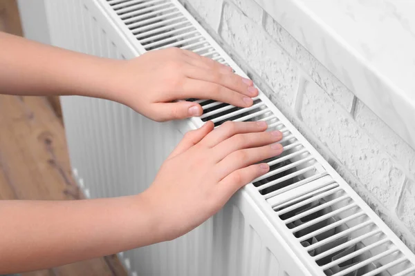 Girl warming hands on heating radiator indoors, closeup
