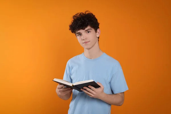 Portrait of teenage boy with book on orange background