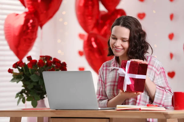 Valentine\'s day celebration in long distance relationship. Woman holding gift box while having video chat with her boyfriend via laptop at home