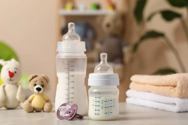 Feeding bottles with baby formula, pacifier, toys and towels on light grey table indoors