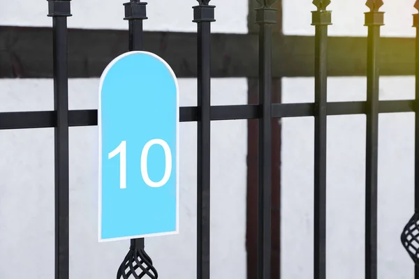 Plate with house number ten hanging on iron fence outdoors