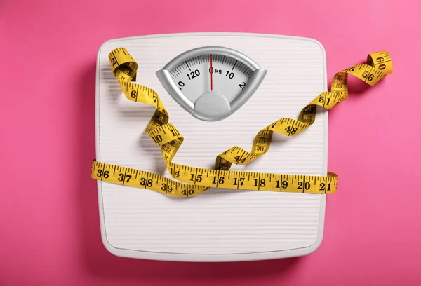 Weight loss concept. Scales and measuring tape on pink background, top view