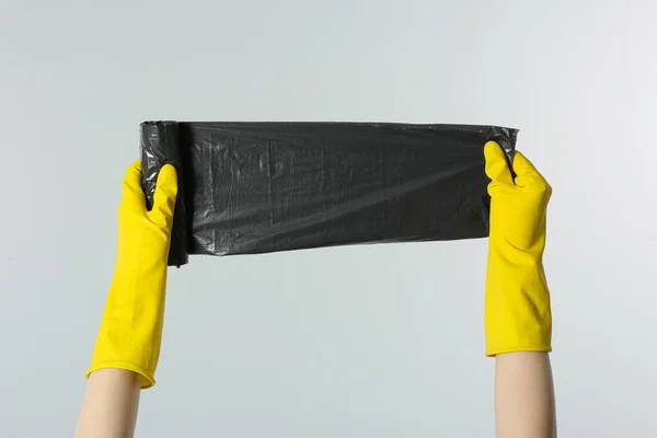 Janitor in rubber gloves holding roll of black garbage bags on light grey background, closeup