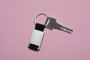 Key with metallic keychain on pale pink background, top view
