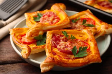 Fresh delicious puff pastry with cheese, tomatoes and parsley on wooden table, closeup