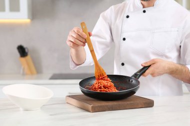 Professional chef with delicious spaghetti at marble table in kitchen, closeup