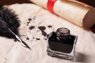 Open inkwell and feather pen on vintage parchment with stains, closeup