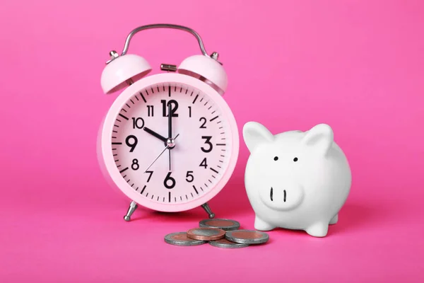 Ceramic piggy bank, coins and alarm clock on pink background. Financial savings
