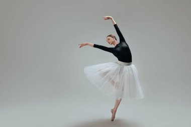 Young ballerina practicing dance moves on light grey background. Space for text