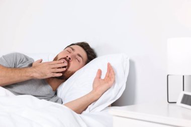 Handsome man yawning while lying on pillow in bed at home