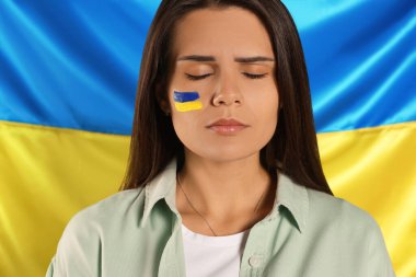 Sad young woman with face paint near Ukrainian flag