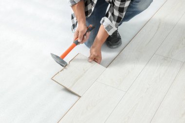 Professional worker using hammer during installation of new laminate flooring, closeup