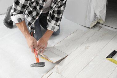 Professional worker using hammer during installation of new laminate flooring indoors, closeup
