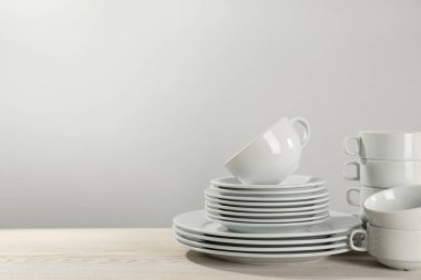 Set of clean dishware on white wooden table against light background. Space for text