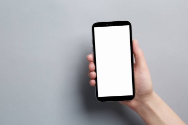 Woman holding smartphone with blank screen on grey background, closeup. Mockup for design