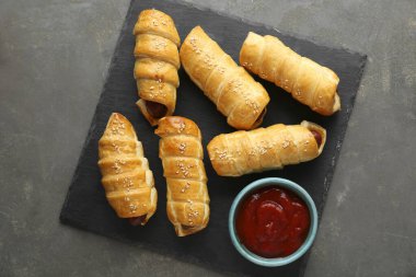 Delicious sausage rolls and ketchup on grey table, top view