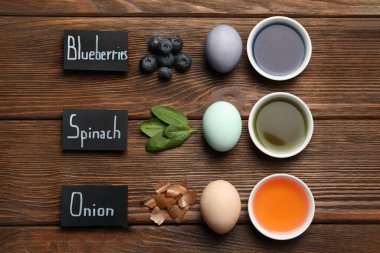 Easter eggs painted with natural organic dyes and labels on wooden table, flat lay. Blueberries, spinach, onion used for coloring