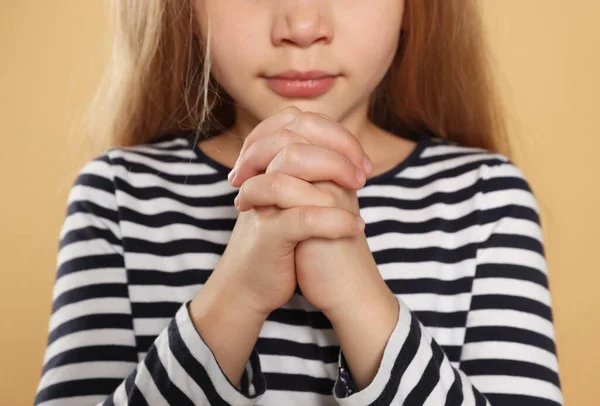 Girl with clasped hands praying on beige background, closeup