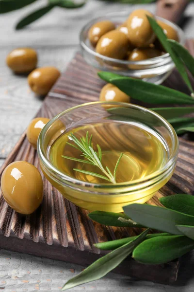 Bowl of cooking oil, olives and green leaves on wooden table