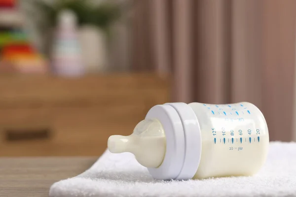 Feeding bottle with baby formula and soft towel on wooden table indoors. Space for text