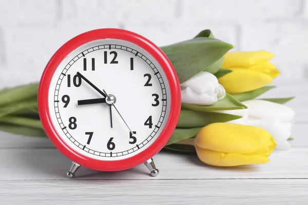Red Alarm Clock Beautiful Tulips White Wooden Table Brick Wall — Stok fotoğraf