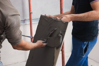 İşçi spatulayla karo üzerine yapıştırıcı yayıyor, yakın plan.