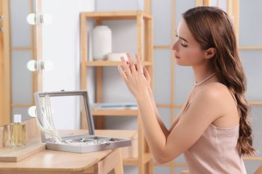 Young woman trying on elegant ring with pearls indoors