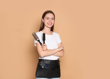 Portrait of happy hairdresser with brushes on beige background. Space for text
