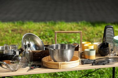 Many different kitchen items on wooden table outdoors. Garage sale