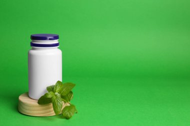 Plastic medicine bottle and leaves on green background, space for text. Medicament