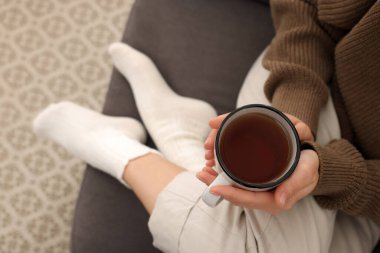 Woman in warm socks relaxing with cup of tea at home, above view