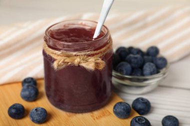 Jar of delicious blueberry jam and fresh berries on white wooden table, closeup