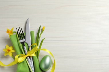 Cutlery set, painted egg and beautiful flowers on wooden table, flat lay with space for text. Easter celebration
