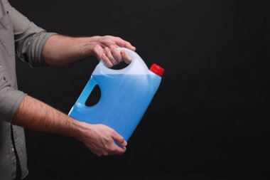 Man holding canister with blue liquid on black background, closeup. Space for text