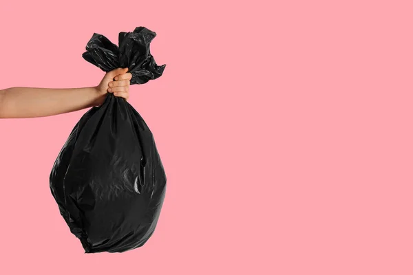 Woman holding trash bag full of garbage on pink background, closeup. Space for text