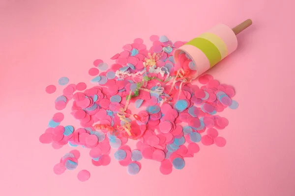 Colorful confetti, serpentine and party popper on pink background