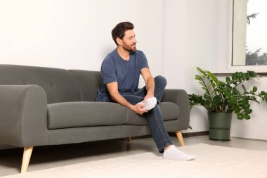 Man suffering from leg pain and massaging heel on sofa at home