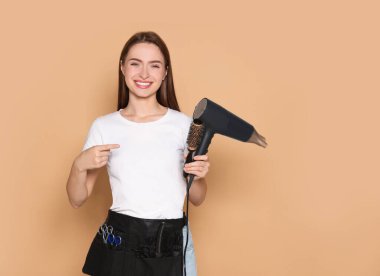 Portrait of happy hairdresser with hairdryer and brush on beige background. Space for text